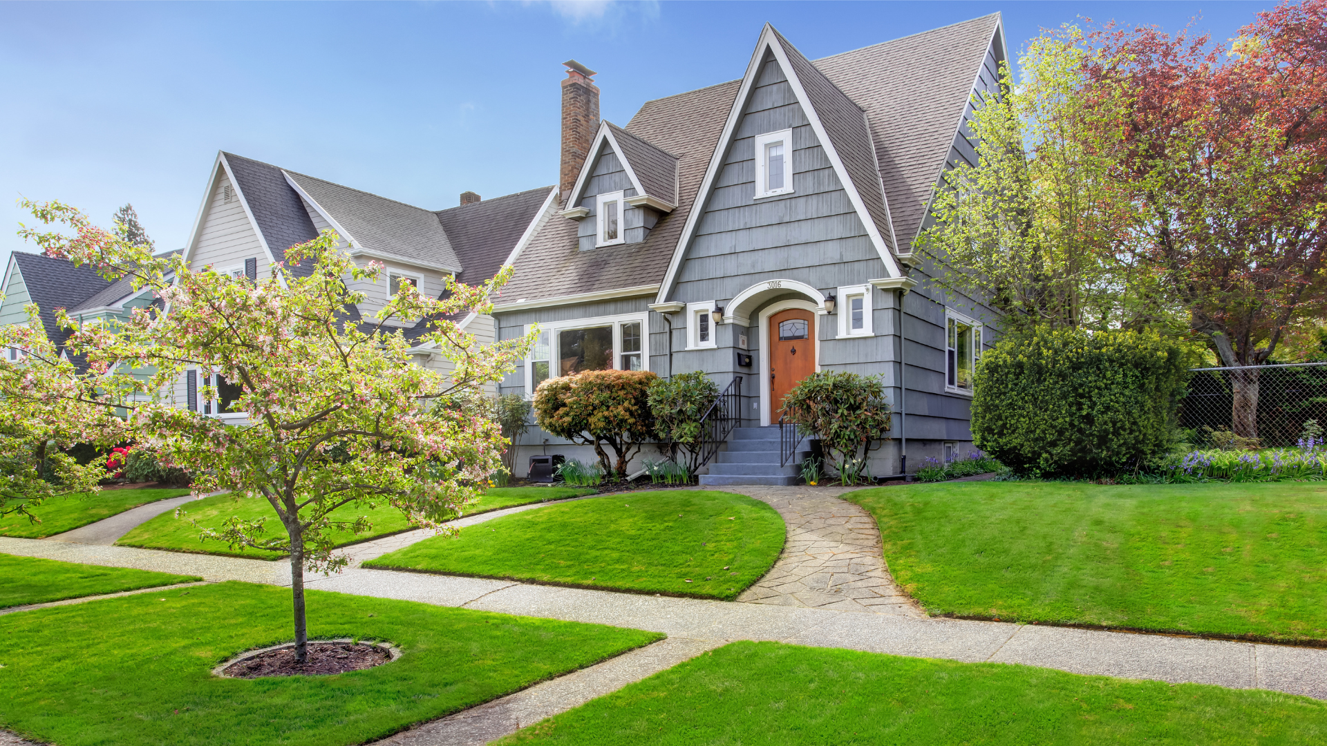 Gray Craftsman-style home with a landscaped front yard, blooming tree, and curved walkway leading to the front entrance.